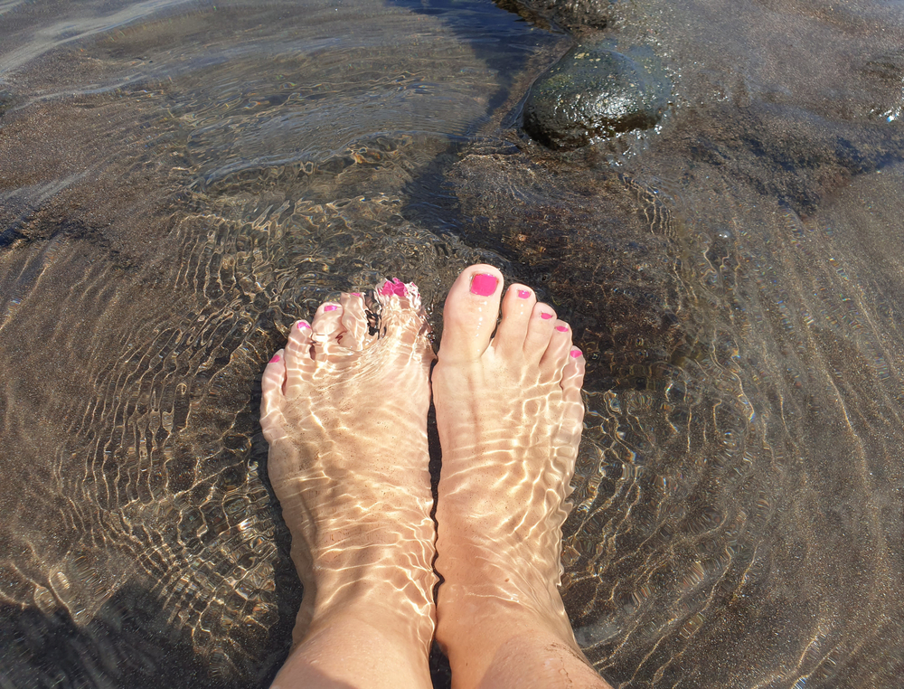 Feet with fresh pedicure resting in clear shallow water