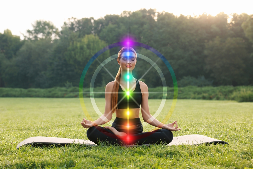 Woman meditating outdoors with the seven chakras illuminated during a chakra balancing session